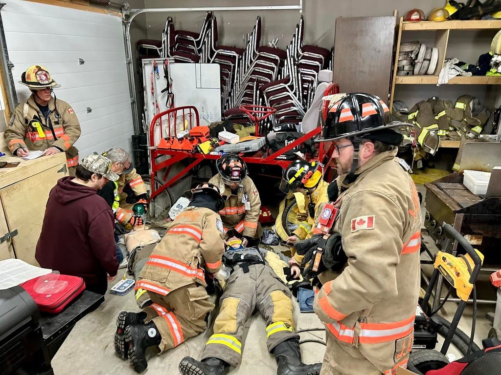 Firefighters in turnout gear practise treating an injured crew member during a training night